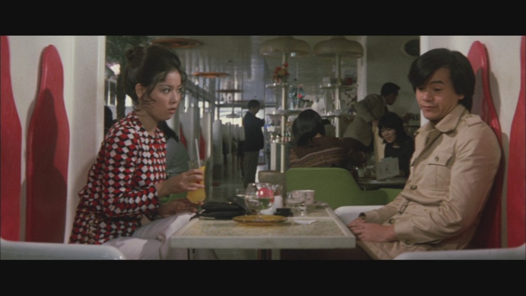 Young woman with red white and black patterned dress sits across from young man with hip coat