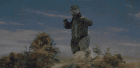 Godzilla entering with a pep in his step, pumping his arms while walking