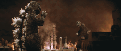 One Godzilla fires atomic breath at another Godzilla amid a burning oil refinery