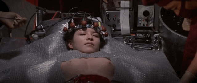 Katsura being operated on with mechanical gears and wires exposed, as well as a pair of fake breasts