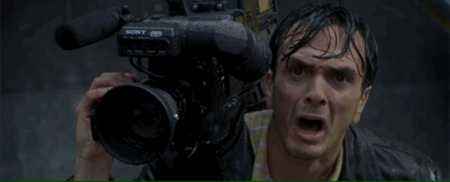 A man with a TV Camera stands in the street as Godzilla's foot stomps down, barely missing him between the toes.