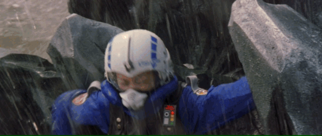 A blue uniformed woman climbs onto Godzilla's scales, shooting a tracker into them as the camera pans up and out showing Godzilla's size