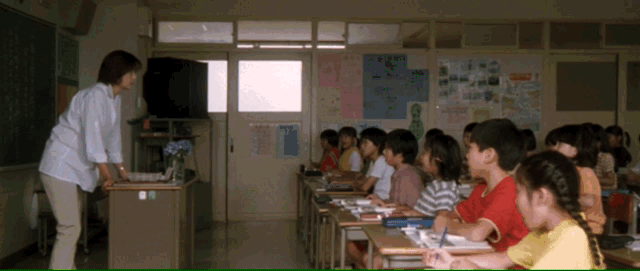 A classroom full of children see a flash from off camera, the building shakes, and the teacher slowly approaches a window to reveal a massive mushroom cloud