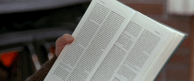 A man sits in a chair holding a book up covering his face, then lowers it to reveal a familiar character